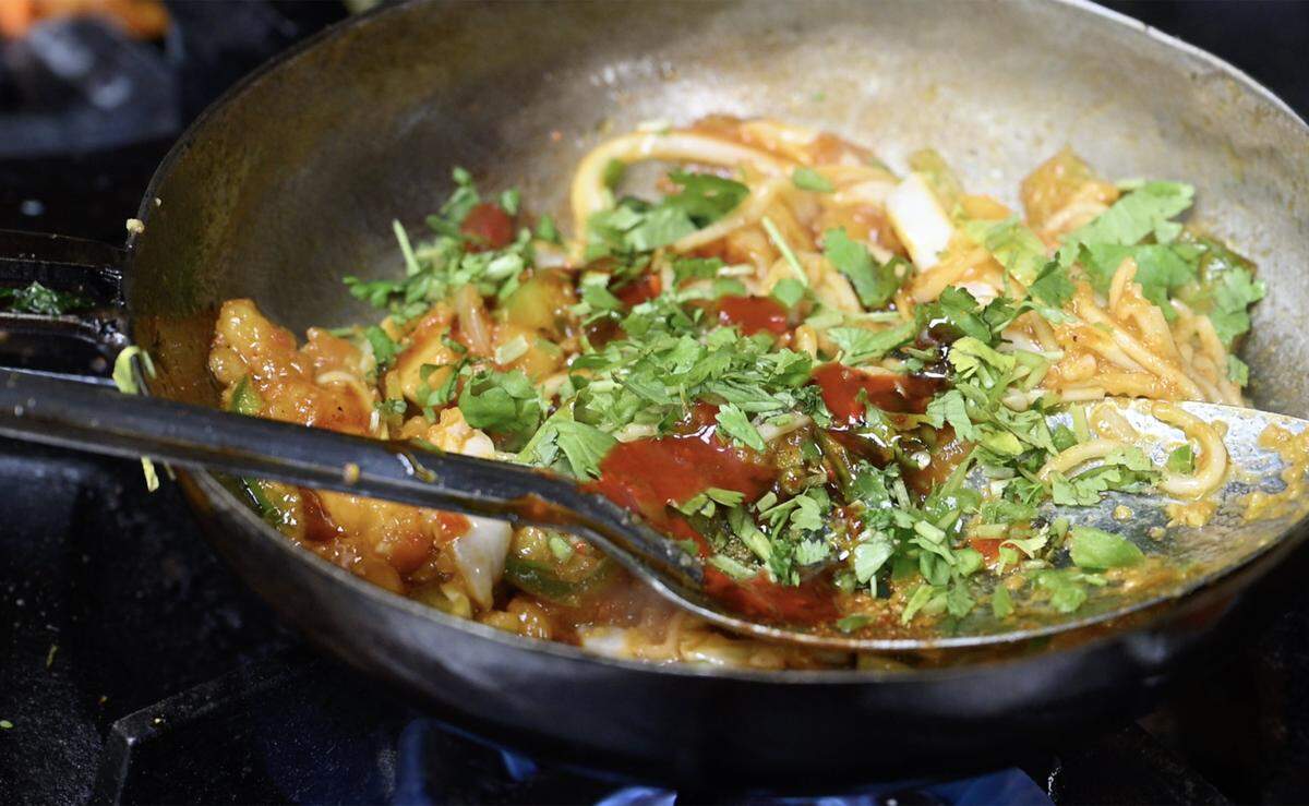 Cilantro is added to the pan as a mixture is cooked for an Aloo Tikka Noodle Burger at Rangla Punjab Restaurant & Sweets Friday, Oct. 17, 2025 in Fresno.