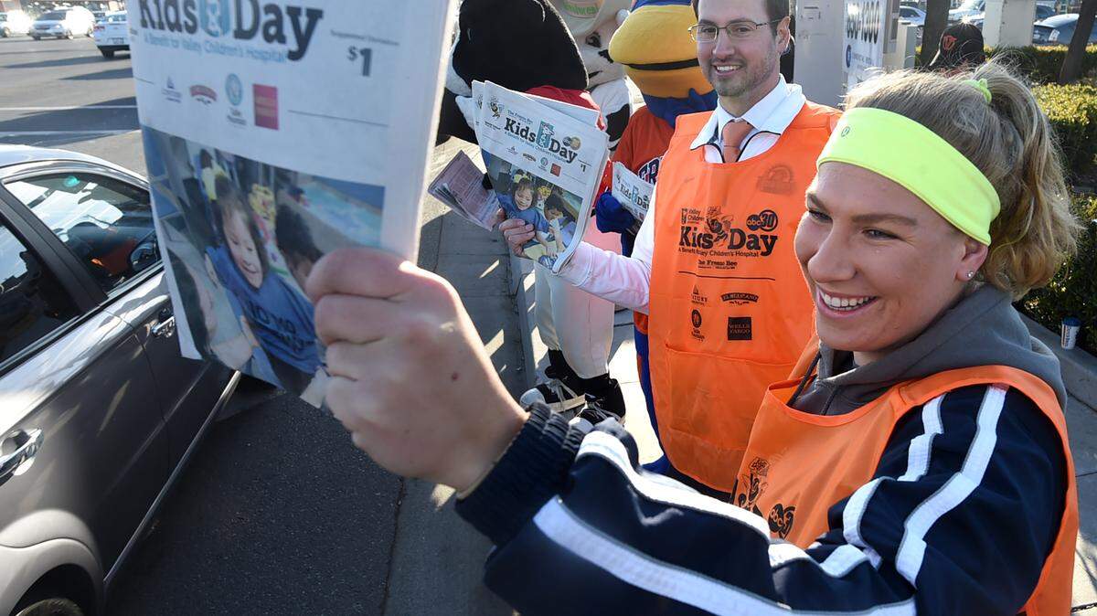 Fresno Pacific University swimmer Hannah Freeman, with Fresno Pacific Athletic Director Aaron Henderson, center, sell Kids Day papers at Blackstone and Shaw avenues Tuesday morning, March 6, 2018.