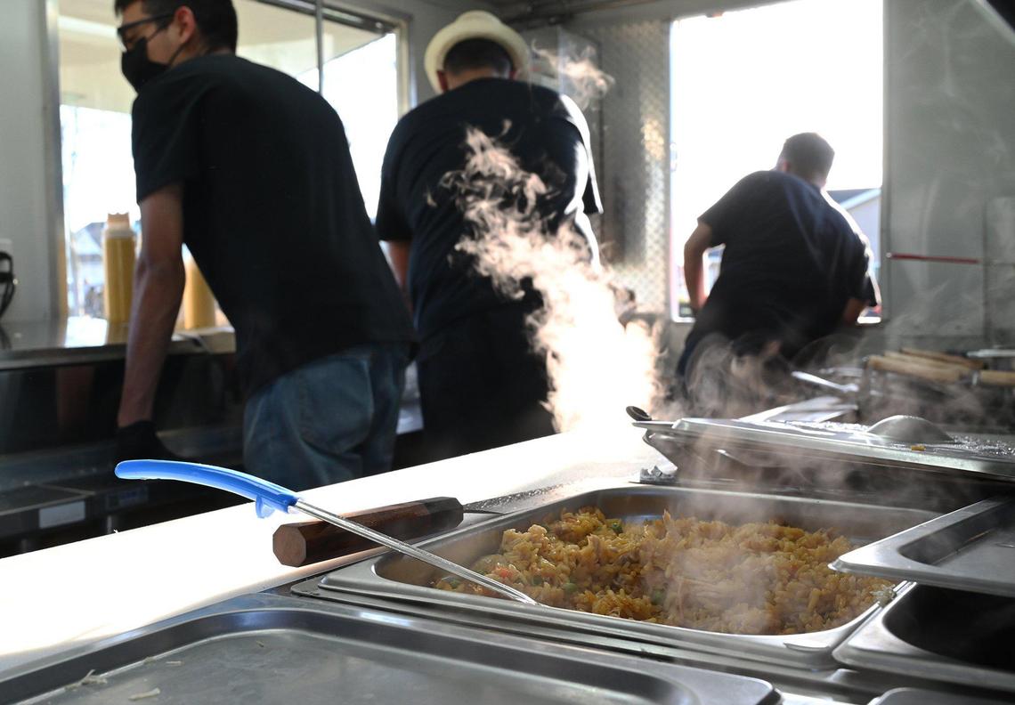 Steam rises from saffron rice as Lazaro and Niermin prepare to begin serving Cuban food at their new food truck Havana Cafe with help from family members at a community park Wednesday, March 16, 2022 in Fresno.