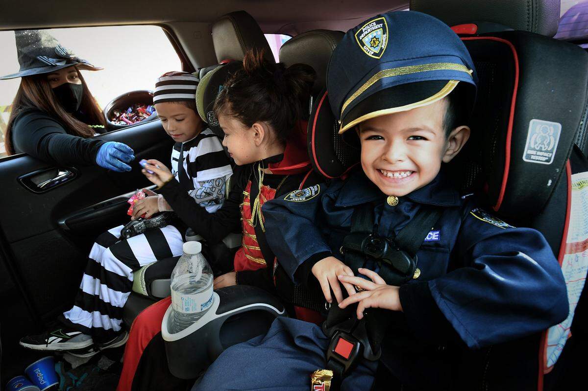 Dressed as a police officer, West Park Elementary preschooler Nathan Aguilar beams as he waits patiently for his candy from school staffer Kristin Young, left, dressed as a witch, who hands it out to his brother, Cesar Aguilar, kindergartner, and sister, Alexis Aguilar, fourth-grader, Monday during the school’s Halloween Drive Thru Costume Parade in 2020.