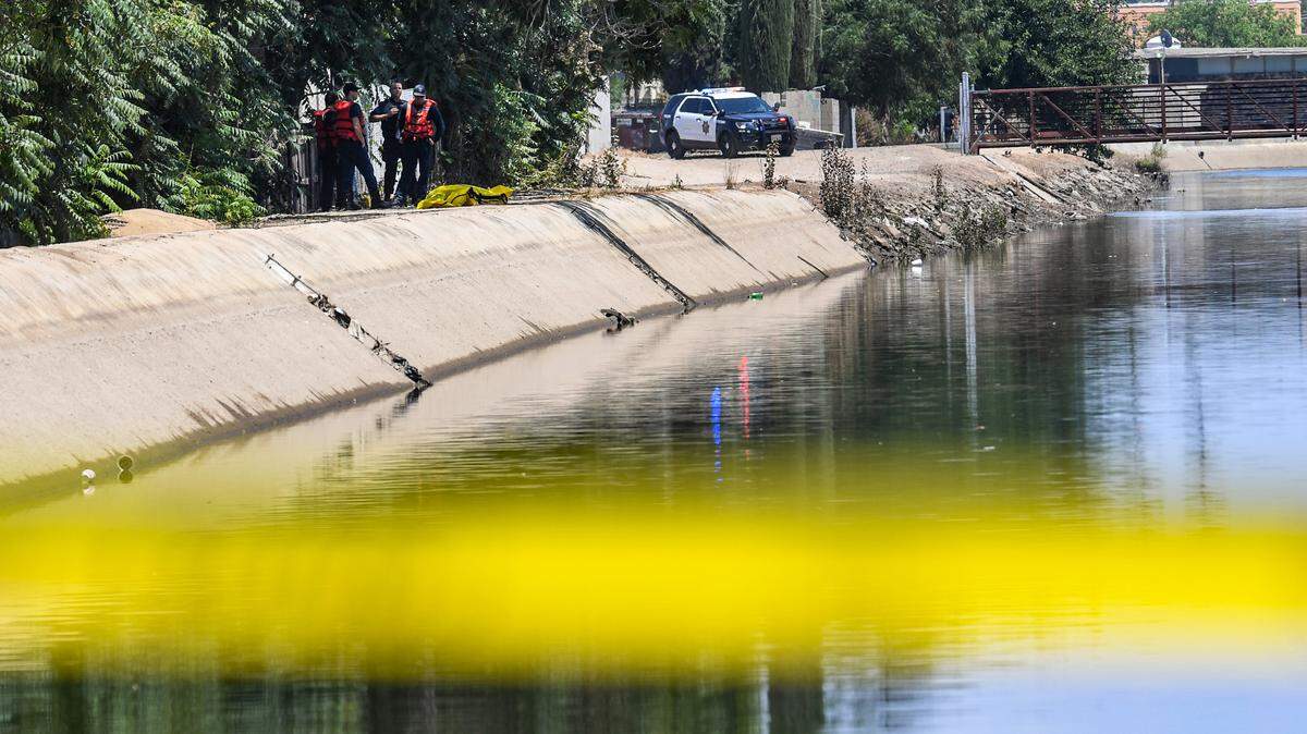 Police and rescue personnel stand on the bank of the canal near Maroa and Dayton avenues in Fresno after recovering the body of a man floating in the water on Thursday, July 1, 2021. Officers are investigating the cause.