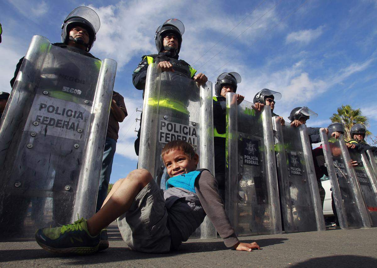 A young boy with the group of Central American migrants that marched from a shelter to the border in order to apply for asylum in the United States, sits in front of a line of Mexican federal police officers as the officers prevent the migrants from getting any closer to the Mexican-U.S border in Tijuana, Mexico on Thursday, Nov. 22, 2018. (Hayne Palmour IV/San Diego Union-Tribune/TNS)