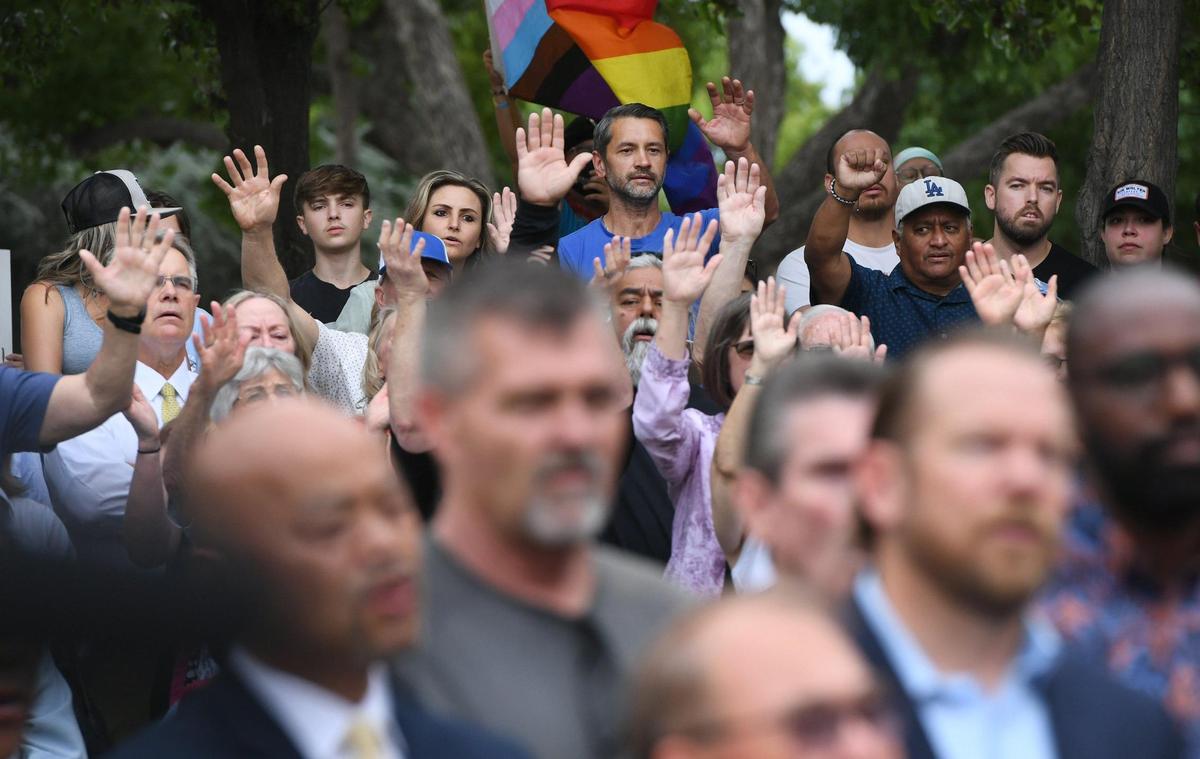 Supporters of local churches raise their hands asa Pride flag is seen in the far background as Cornerstone Church, Adventure Church and others hold a press conference at Eaton Plaza against the recent Pride flag raising at Fresno City Hall Tuesday, June 22, 2022 in Fresno.