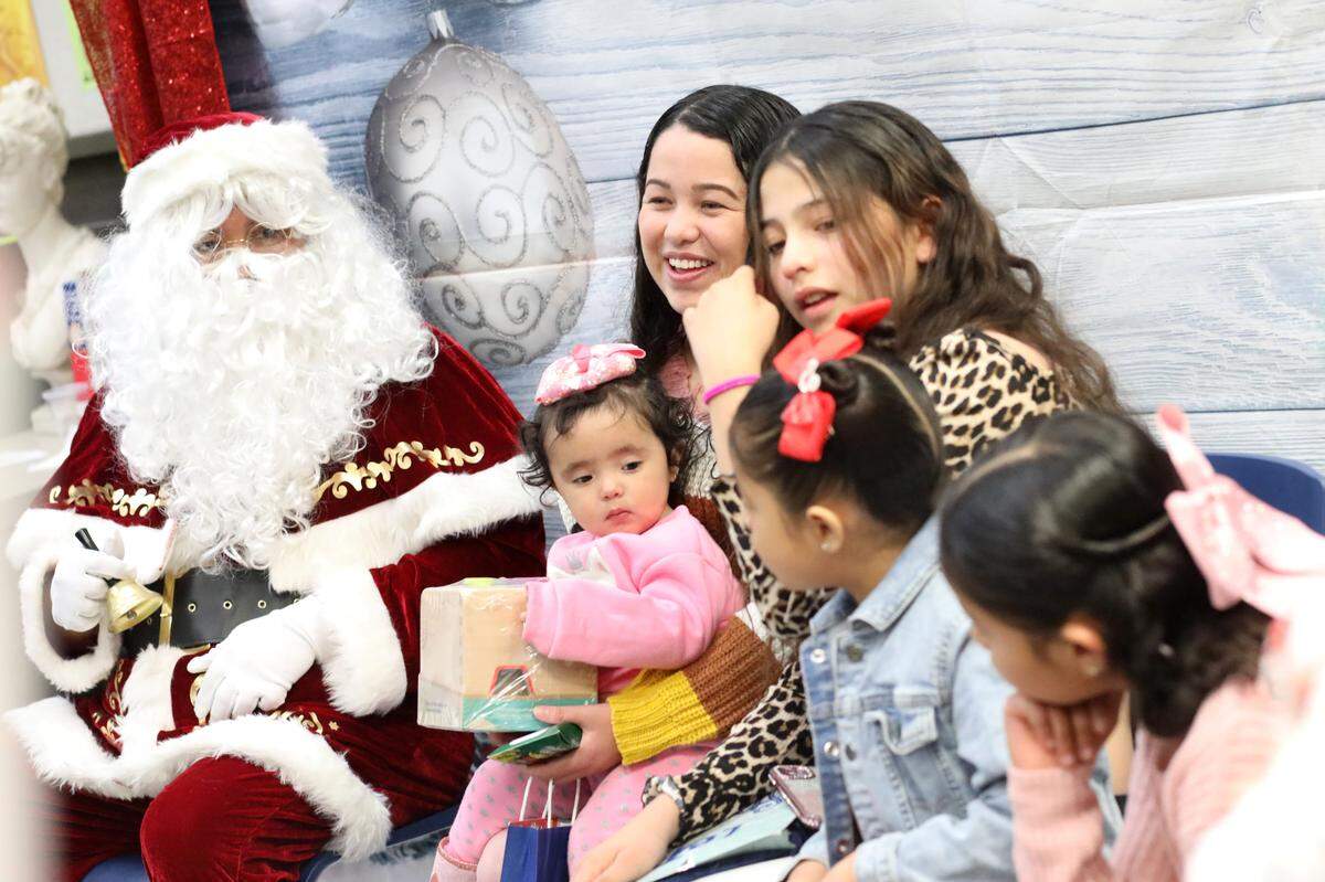 Isela Molina with her children and Santa smiles during the 2023 Migrant Family Christmas event that took place at Firebaugh High School library on Dec. 13.