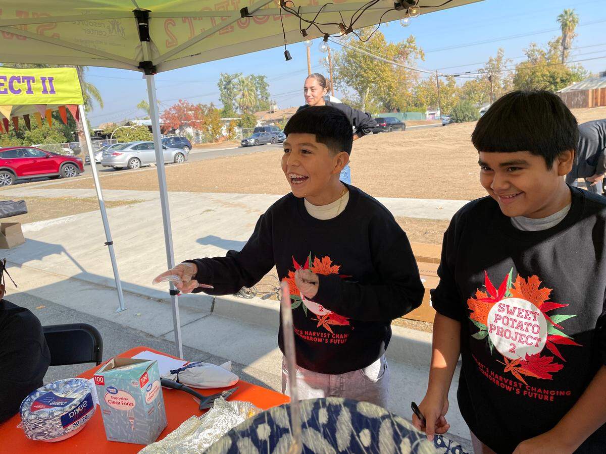 Sweet Potato Project participant Ismael Pacheco, left, laughs with festival attendees as he prepares to serve sweet potato cinnamon rolls on Saturday, November 12, 2022.
