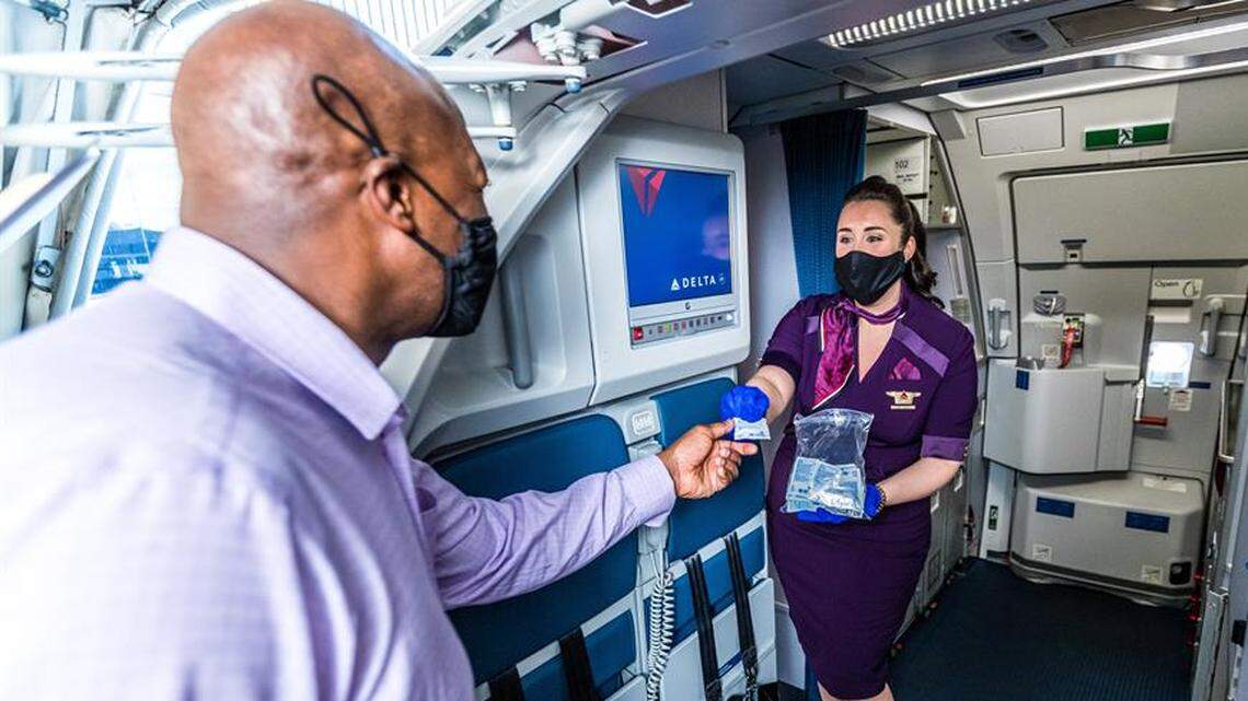 A Delta Air Lines flight attendant in a face mask give a packet of hand sanitizer to a passenger boarding one of the carrier’s flights.