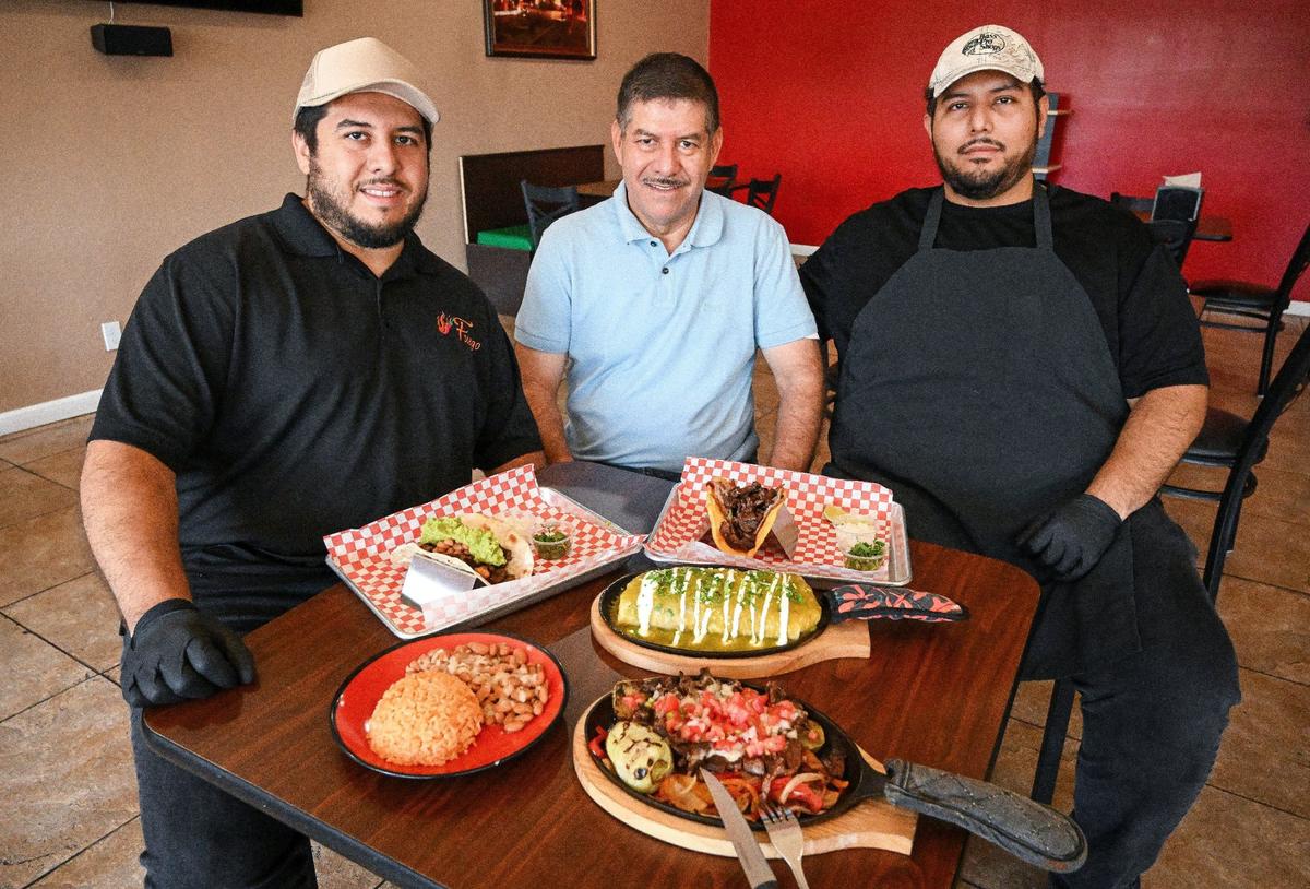 Aldo Ramirez, left; his brother Anton Ramirez, right, and their father, Javier Ramirez, sit with plates of food including nopal montado, taco perron, taco el jefe and a wet burrito with al pastor at Fuego Taqueria y Restaurante in Fresno. All three own the restaurant.