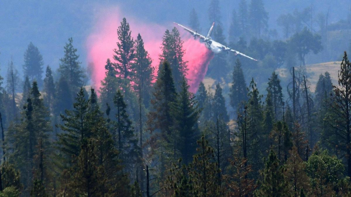 Viewed from about a mile away and through heat waves, a fire tanker drops a load of retardant on the Blue Fire, south of Shaver Lake, June 30, 2021.