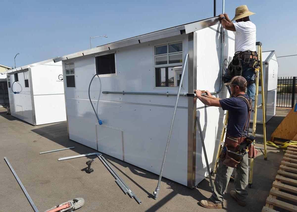 Workers Matthew Jennings, bottom, and Felix Sanchez install electrical on one of the 30 new, state-of-the-art pallet shelters designed and built by people with life experience as homeless individuals, for the Mike McGarvin Jr. Village of Hope Renovation project at the Poverello House, Wednesday Sept. 23, 2020. These will replace the Tuff Sheds that have been used for housing for almost two decades.