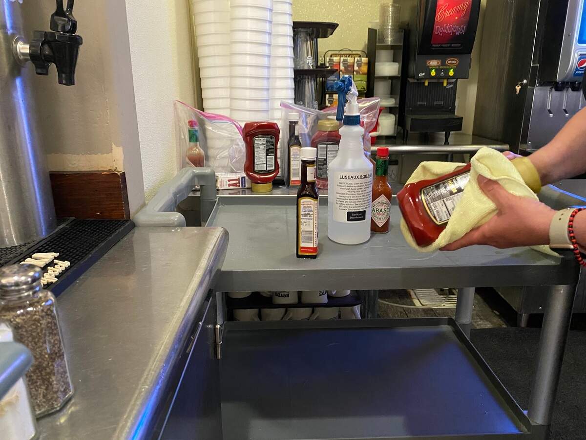A restaurant worker disinfects a ketchup bottle after the party leaves, as required by the new reopening rules.