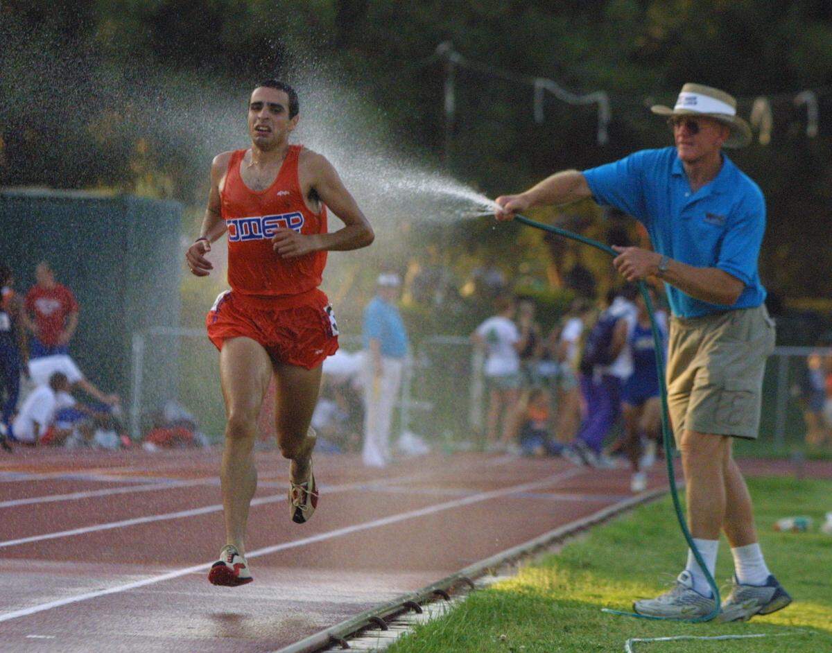 Former Fresno State track and field coach Red Estes hoses off runners during the 3,000-meter race during a blazing hot May day in 2021. Estes died Wednesday, Sept. 29, 2021.