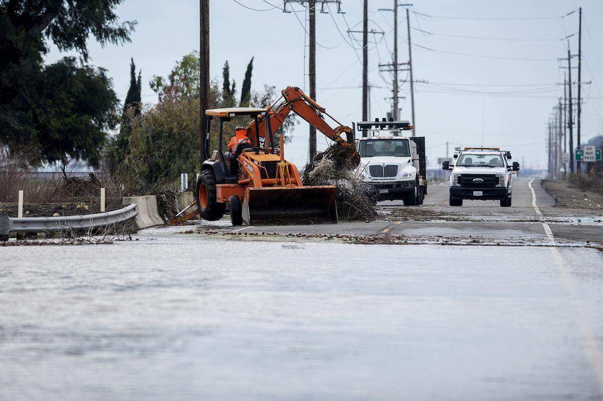 Caltrans crews work to remove debris from Mariposa Creek as floodwater covers a section of Highway 59 in Merced County, Calif., on Monday, Jan. 2, 2023.