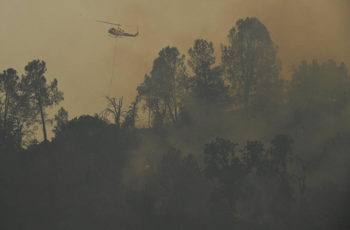 A helicopter hovers over a ridge before dropping a bucket of water as the River Fire grows to 9,000 acres with 10% containment Monday, July 12, 2021, near Coarsegold.