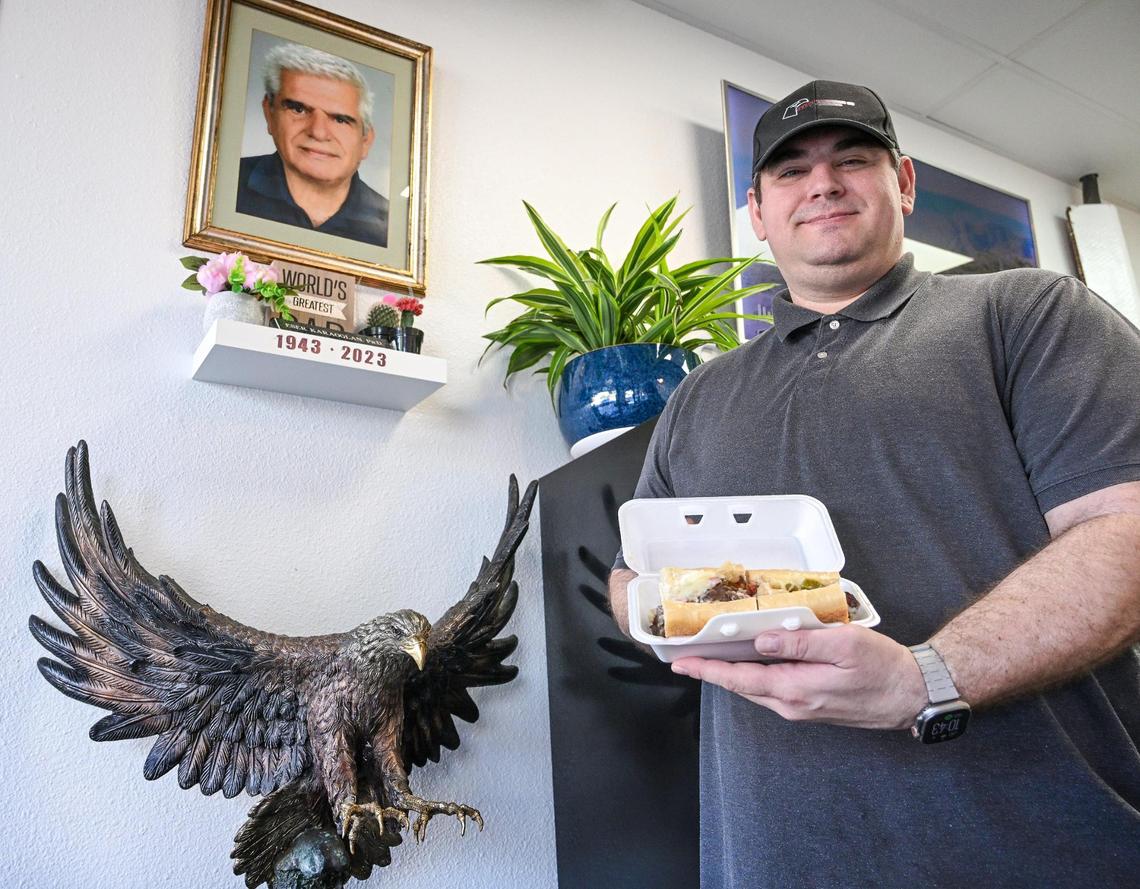 Arnold Karaoglan, owner of the Eagle Sandwich Co., stands with a sandwich near a tribute to father, Eser Karaoglan, who helped him finance the business.