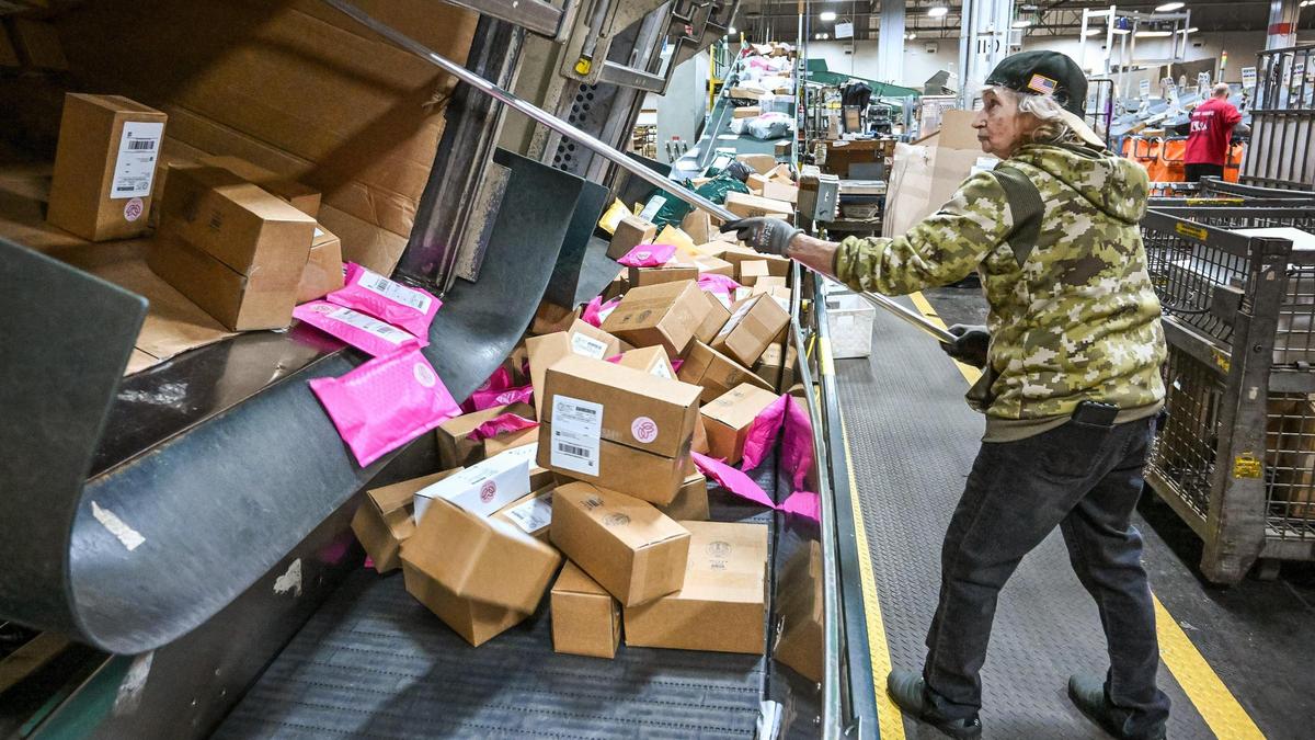 Jolynn Shain pulls parcel packages onto a conveyor belt while working late at the United States Postal Service’s Fresno Mail Processing and Distribution Center on E Street in Fresno on Thursday, Dec. 12, 2024. Workers at the facility handle millions of pieces of mail and packages during the holiday season.