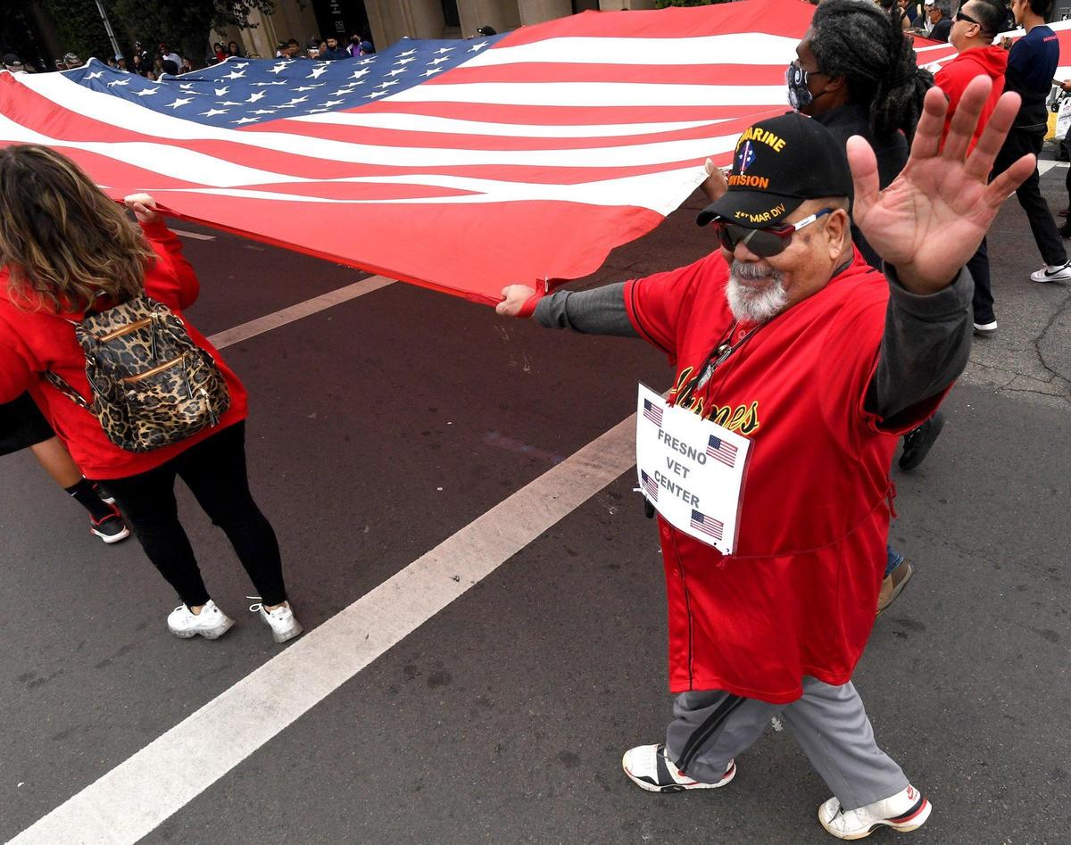 Vietnam War veteran Jose Lopez of the Fresno Vet Center waves to the crowd as he helps carry a giant flag during the Central Valley Veterans Day Parade, Thursday Nov. 11, 2021.