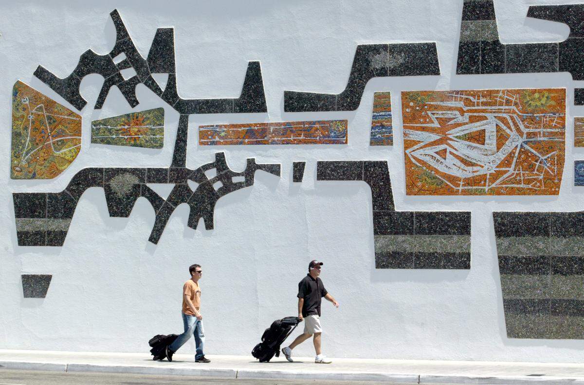 A pair of outgoing travelers walk past the large mural outside the terminal building at the Fresno Yosemite International Airport on their way to catch a flight.