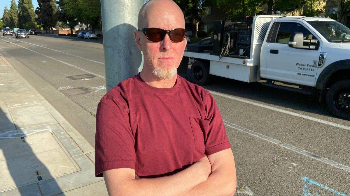 Northeast Fresno resident Justin Palm stands against one of the city-owned streetlight poles containing Verizon 5G short-cell antennas that he blames for emitting a low-frequency hum that has disturbed his sleep since December 2020.