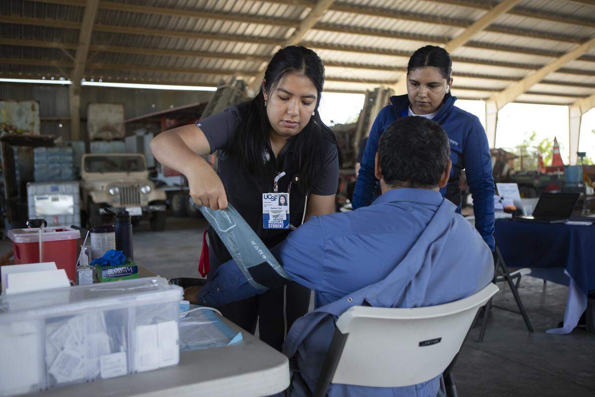 UCSF-Fresno Medical Student Darlene Tran checks the blood pressure of a farmworker in an equipment barn during part of the Rural Mobile Health program visit at a farm outside of Helm on June 16, 2025. Photo by Larry Valenzuela, CalMatters/CatchLight Local