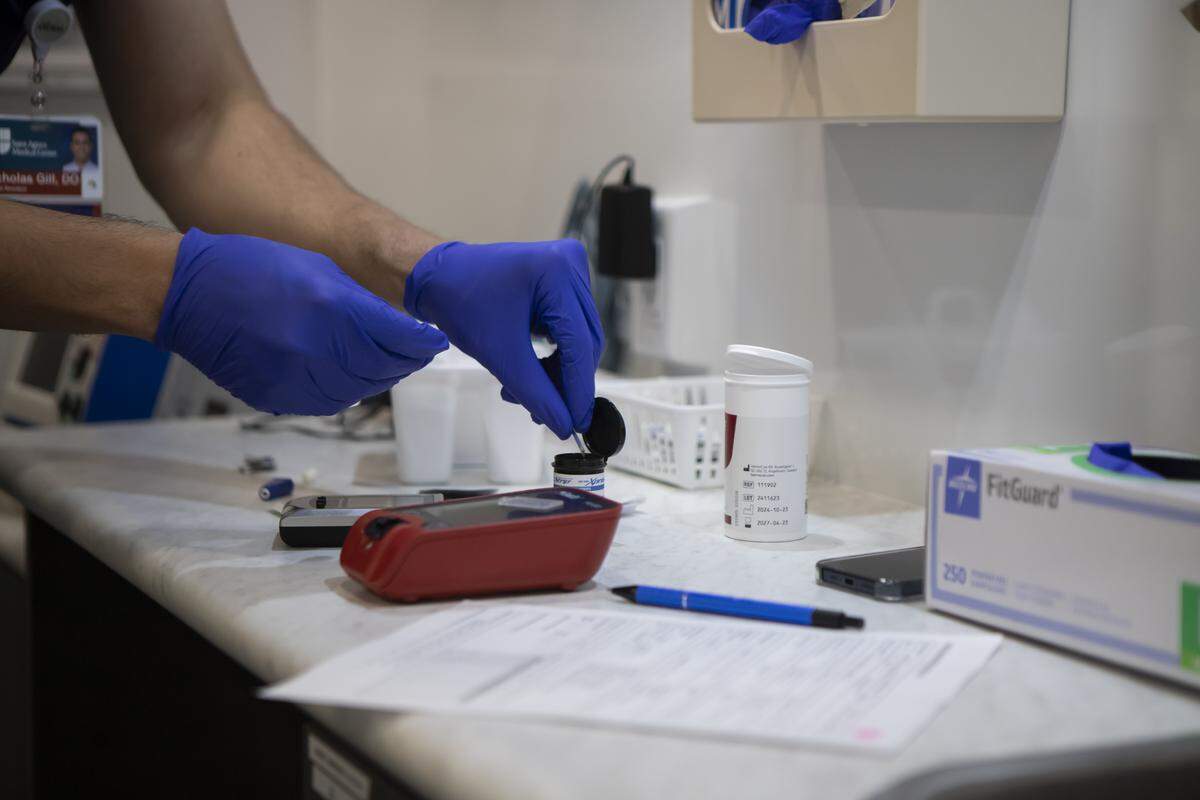 Doctor Nicholas Gill is pulling blood sugar testing strips from a container during a check-up examination in the Saint Agnes Mobile Health Unit mobile clinic, parked in the City Heritage Park parking lot in Parlier on May 16, 2025. Photo by Larry Valenzuela, CalMatters/CatchLight Local
