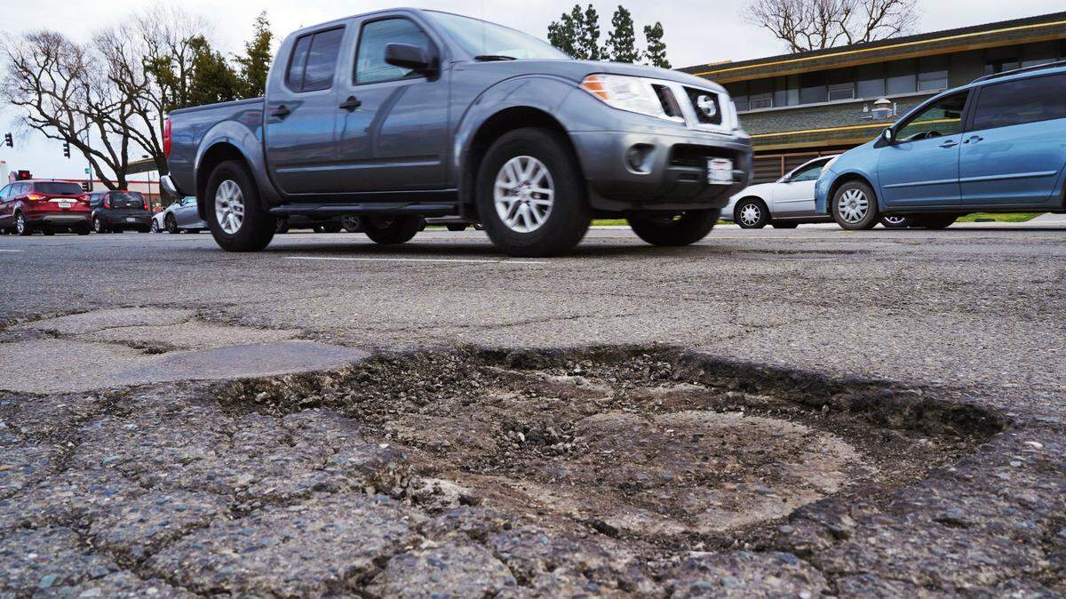 Traffic passes potholes along Ashlan Avenue just west of Blackstone Avenue Wednesday, March 29, 2023 in Fresno. Recent winter storms affected the road conditions.