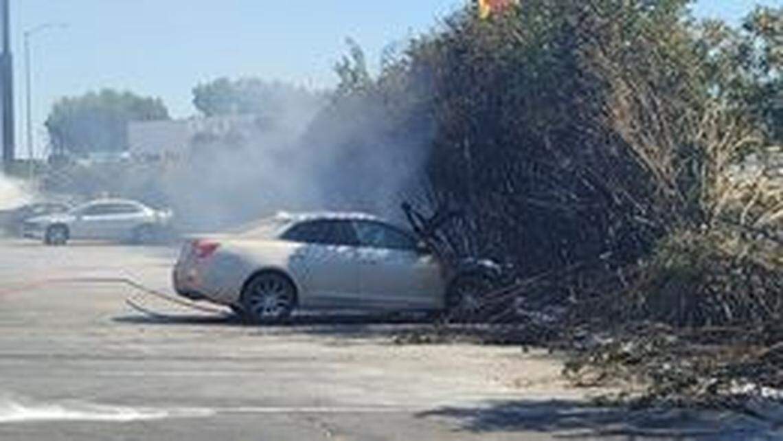 Fire crews work to extinguish flames from a grass fire that spread into the parking lot of a Days Inn, set four vehicles ablaze and left two people hospitalized Sunday, May 30, 2021, in Fresno, California.