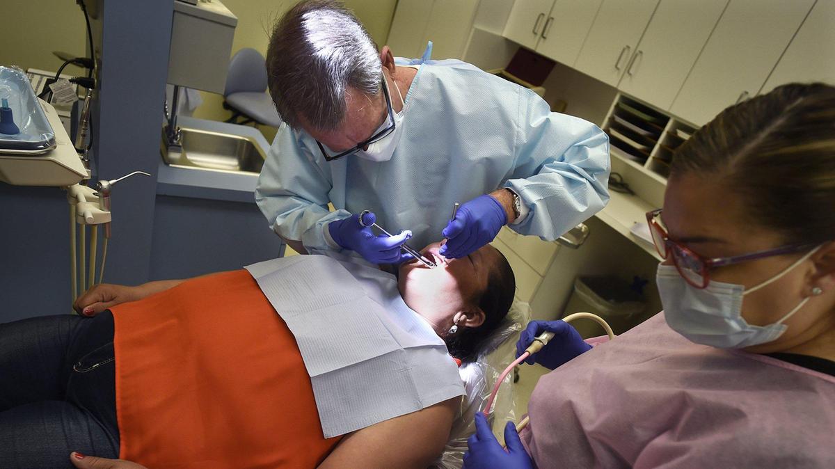 Dr. Richard Jennings treats patient Afrodita Morfin as dental assistant Bertha Gonzalez stands by during one of Jennings’ visits to the Holy Cross Clinic at the Poverello House. Dental health is linked to food security, studies have shown.