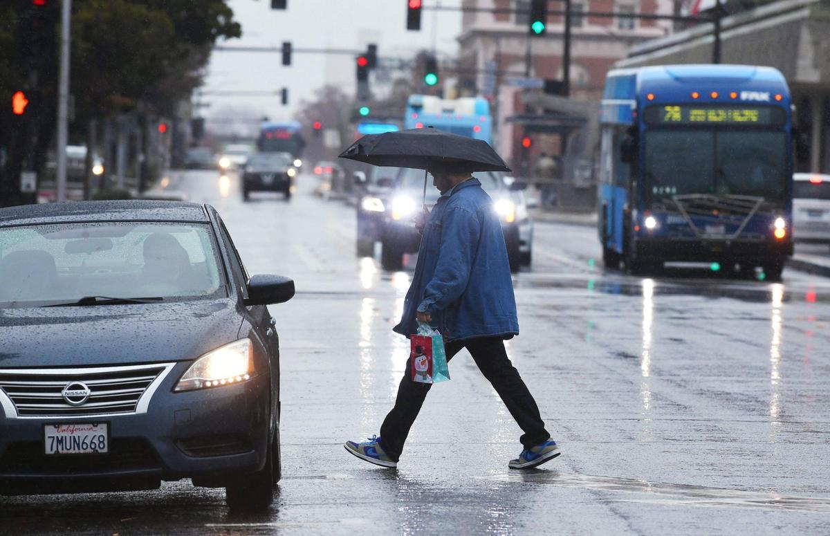 A man crosses Van Ness Ave as rain falls Tuesday morning, Dec. 27, 2022 in downtown Fresno.