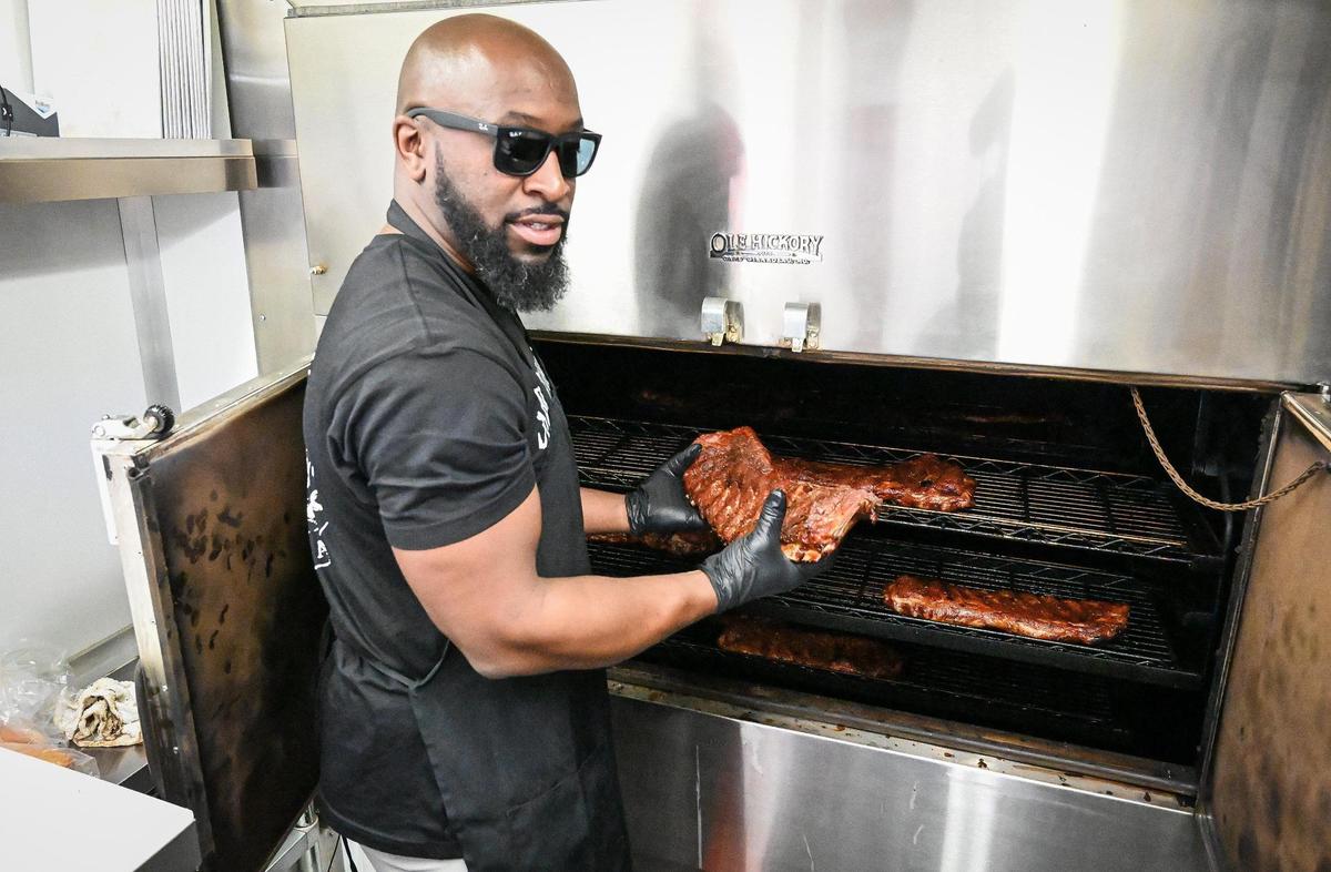 James Woodard pulls off a rack of ribs smoking on the Ole Hickory smoker in the Smoking Woods BBQ food truck in Fresno’s Brewery District in downtown Fresno on Friday, Dec. 9, 2022.
