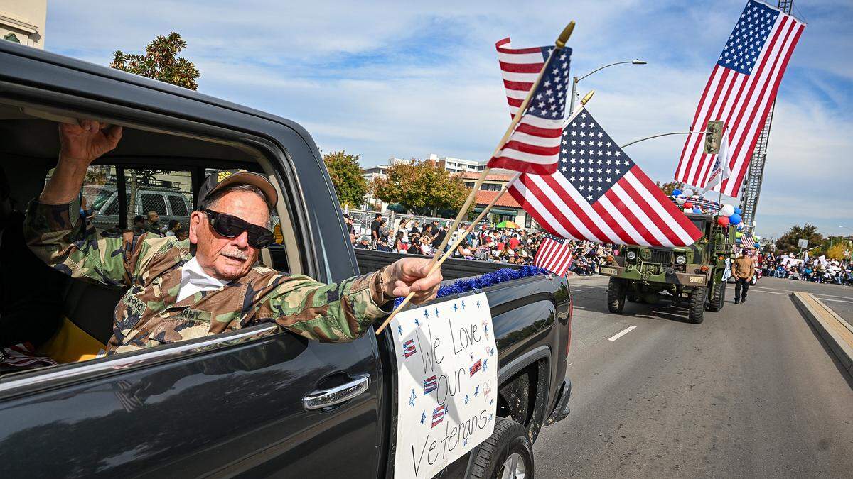 Army and Air Force Veteran Ed Diaz of the VFW Post 8900 waves flags from a vehicle on Veterans Day, his birthday,  while participating in the Central Valley Veterans Day Parade in downtown Fresno on Tuesday, Nov. 11, 2025. 