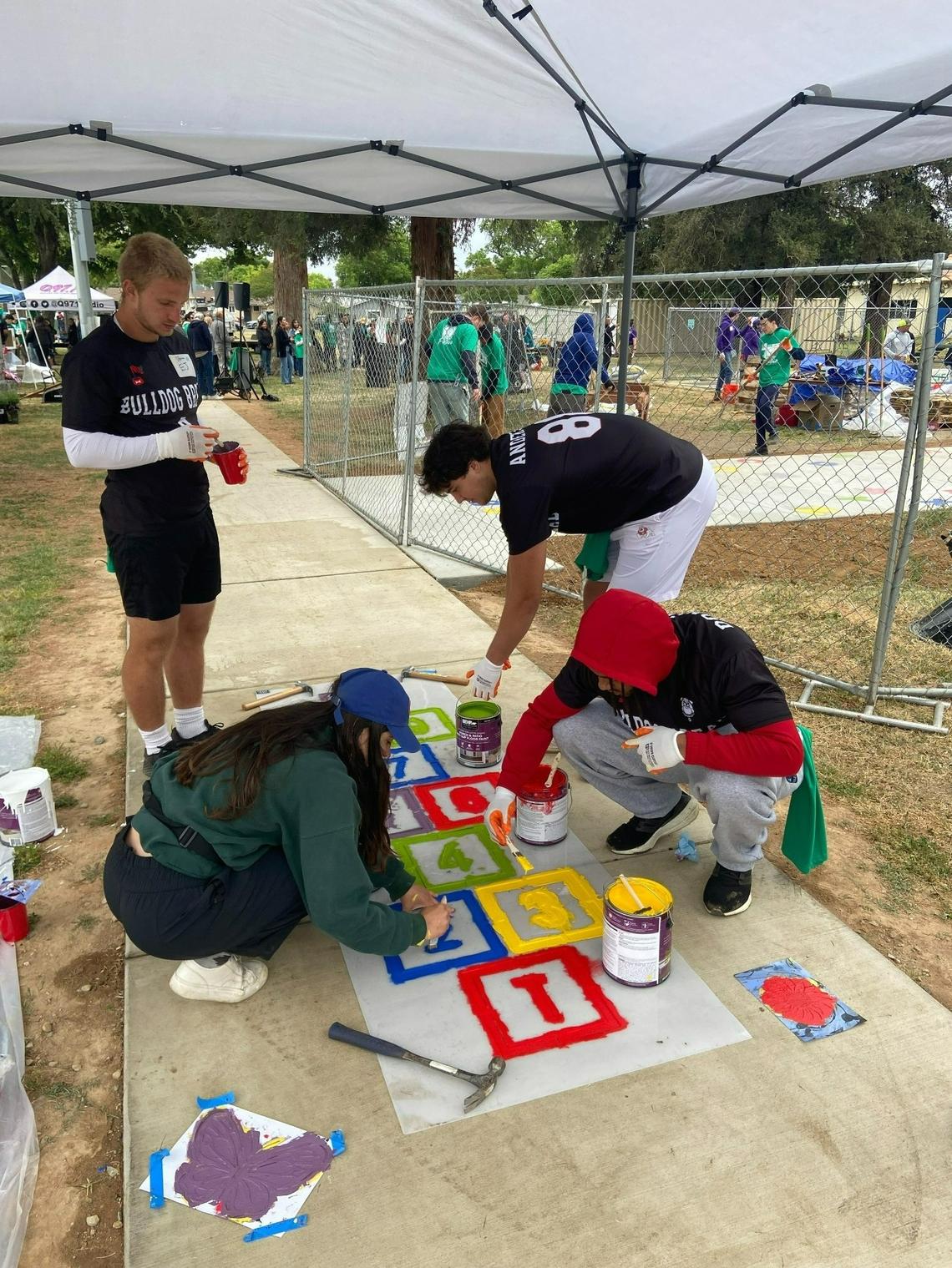 Members of the Fresno State football team including running back Bryson Donelson (front right) use stencils to paint a hopscotch grid on the sidewalk during a community makeover at Cary Park in central Fresno on April 26, 2025.