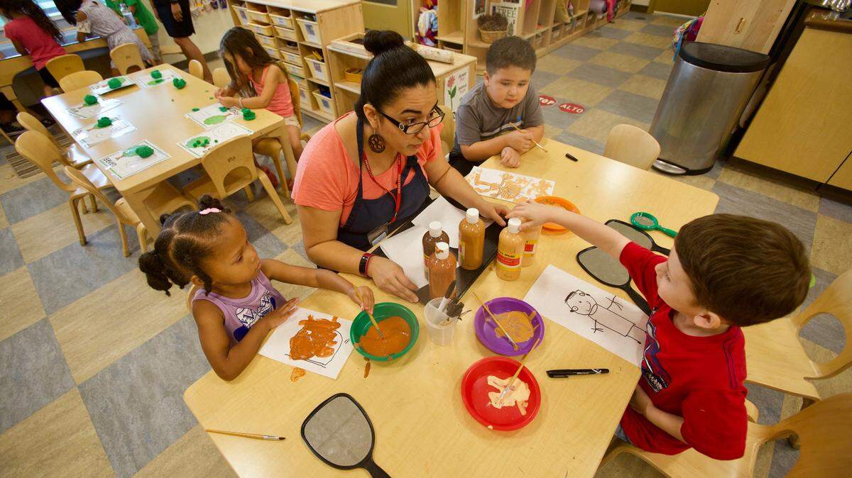 A teacher works with children on their self-portraits, encouraging them to mix paint to determine which color would suit them best at the Lighthouse for Children.