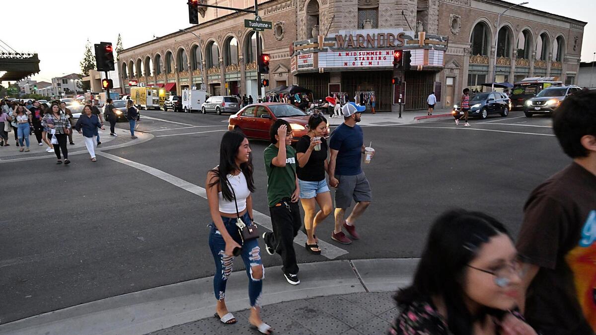 Pedestrians cross in front of the Warnors Center for the Performing Arts, background, on Fulton Street during ArtHop on Thursday, Aug. 3, 2023. City of Fresno’s new deputy chief of staff overseeing downtown revitalization opened a gelato shop in the building last year.
