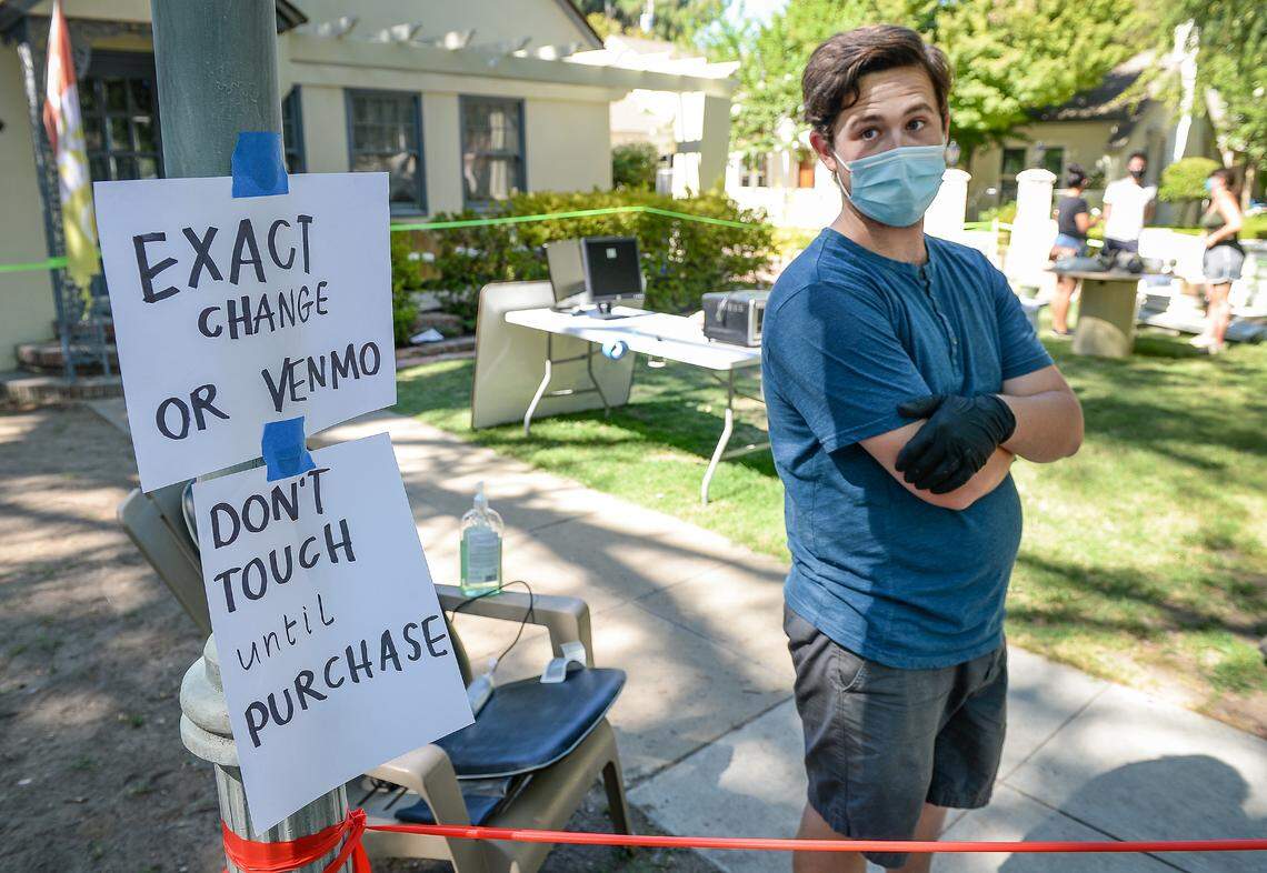 Quentin Sanford, who put up signs meant to help customers keep safe from the spread of the coronavirus, keeps watch over his yard sale during the annual Harvard block sale in Fresno on Saturday, July 11, 2020. The sale was moved from May due to the coronavirus pandemic, but was still discouraged by city officials.