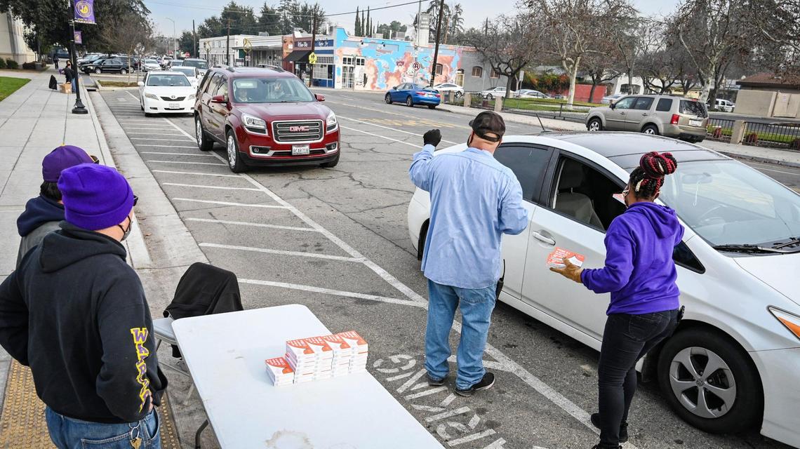 Fresno Unified School District staff members hand out a few remaining COVID-19 test kits to parents in their cars lined up the street in front of Fresno High School on Monday, Jan. 10, 2022.