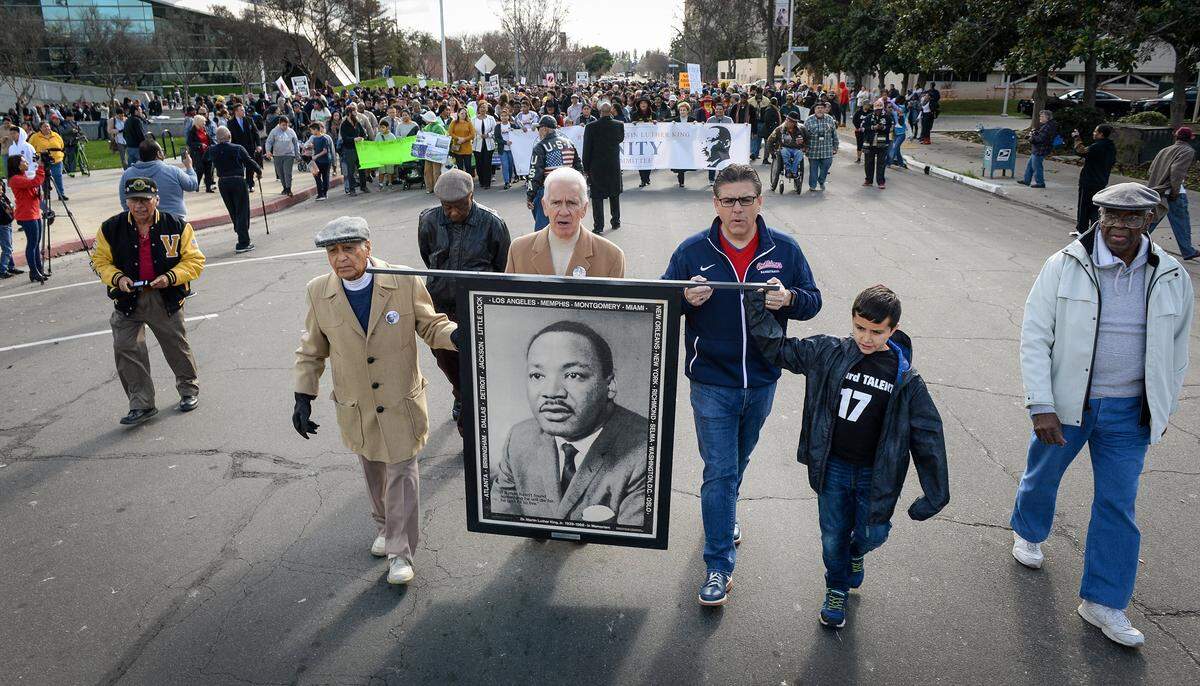 Dr. Sudarshan Kapoor, from left, Congressman Jim Costa, Fresno State President Joseph Castro and his son Jess, 10, help carry a large image of Dr. Martin Luther King Jr. while leading marchers toward the Veterans Memorial Auditorium during the MLK march and commemoration in downtown Fresno on Monday, Jan. 21, 2019.