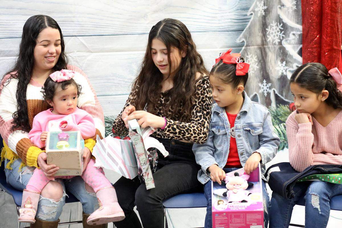 Isela Molina smiles as her 10-year-old daughter Emily Ayala (center) opens a present during the 2023 Migrant Family Christmas event that took place at Firebaugh High School library on Dec. 13.