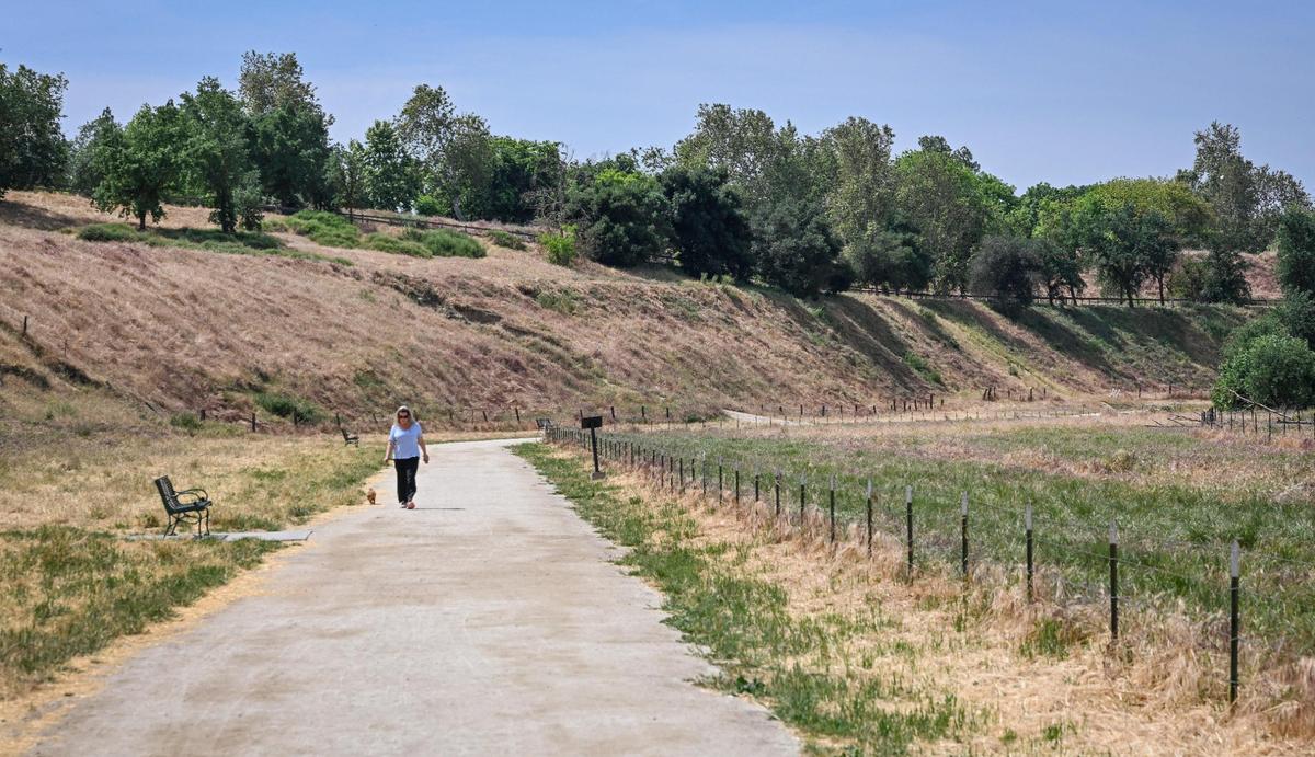 A woman walks her dog along one of the San Joaquin river access trails just below Woodward Park in Fresno on Wednesday, April 20, 2025.
