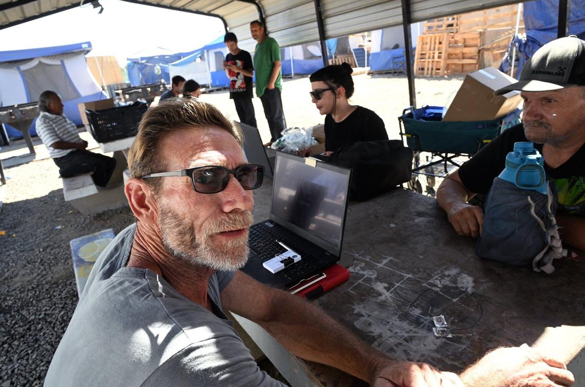 Tom Marchbanks, an alcohol and drug counselor with the Tulare County Health & Human Services Agency, left, sits with other representatives of city agencies and non-profits ready to offer help to residents at the City of Tulare’s temporary encampment. Marchbanks and others said they offer their services every Tuesday. Photographed Tuesday, Sept. 10, 2024 in Tulare.