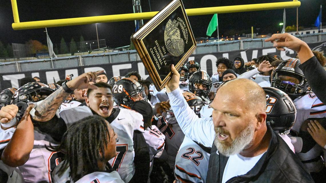 Central head football coach Kyle Biggs, right, holds up the Central Section Division 1-AA football championship trophy as his players celebrate following the Grizzlies victory over Clovis East in the championship game at Lamonica Stadium on Friday, Nov. 22, 2024.