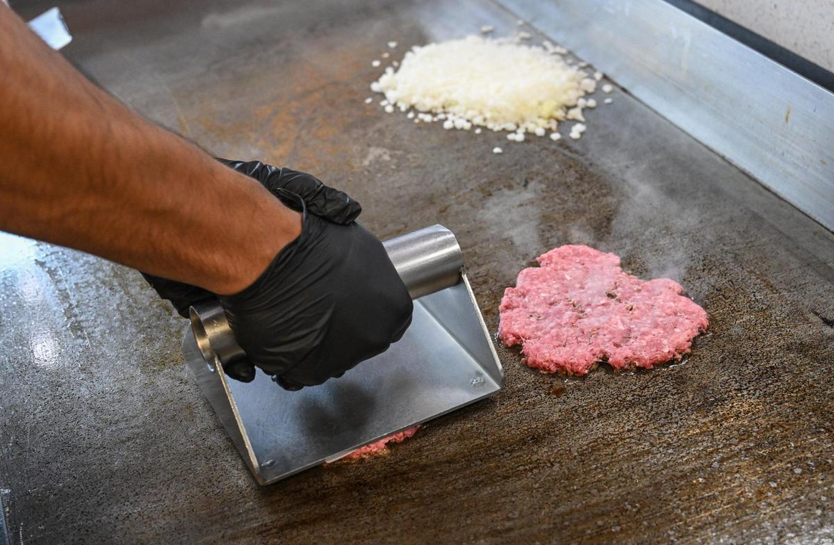 A press is used to flatten hamburger meat on the grill at Main Street Burgers located at the Marketplace at El Paseo in northwest Fresno.