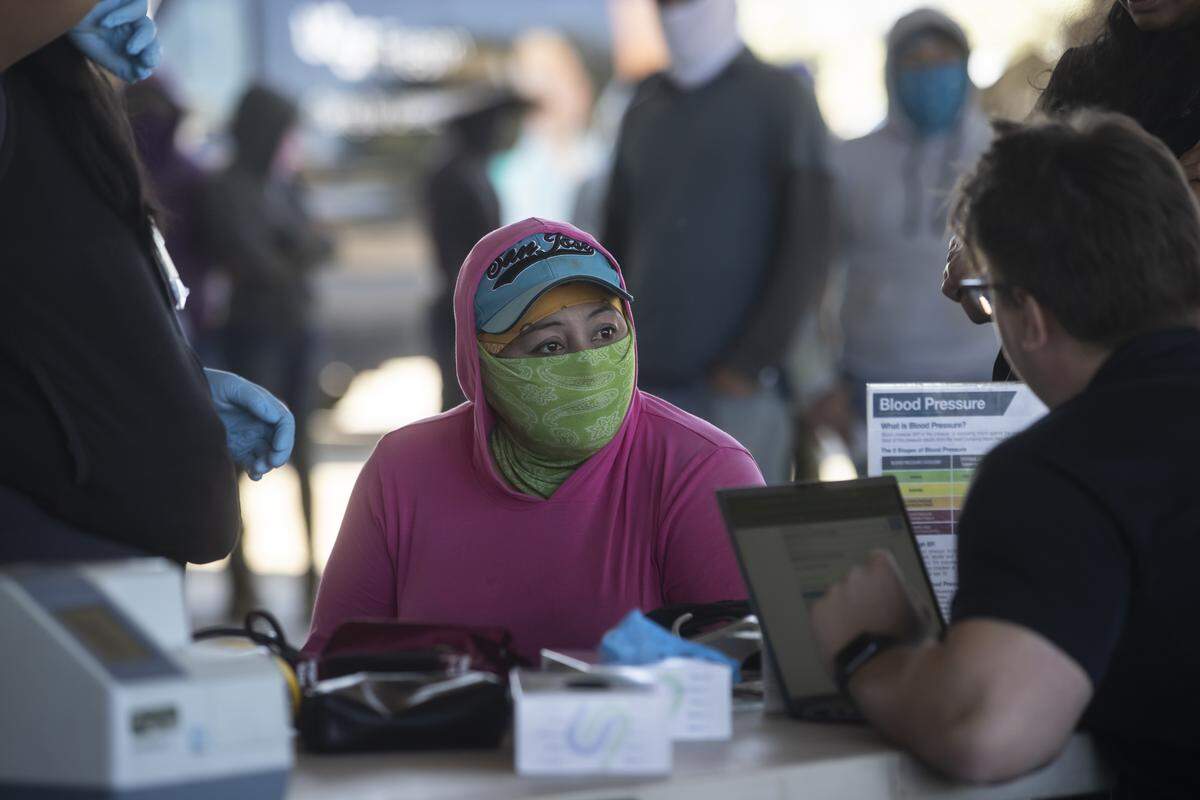 Farmworkers line up in an equipment barn to get a check-up by the staff of UCSF-Fresno, part of the Rural Mobile Health program, at a farm outside of Helm on June 16, 2025. Photos by Larry Valenzuela, CalMatters/CatchLight Local