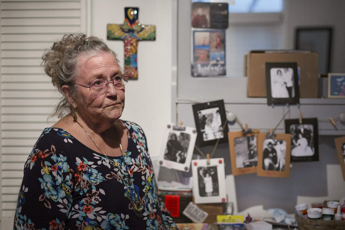 Susan McClellan, 70, with tears in her eyes, stands in front of portraits and photos of her family and husband Harry McCllan, who has passed away. Dec 4, 2021. Photo by Julie Leopo for CalMatters