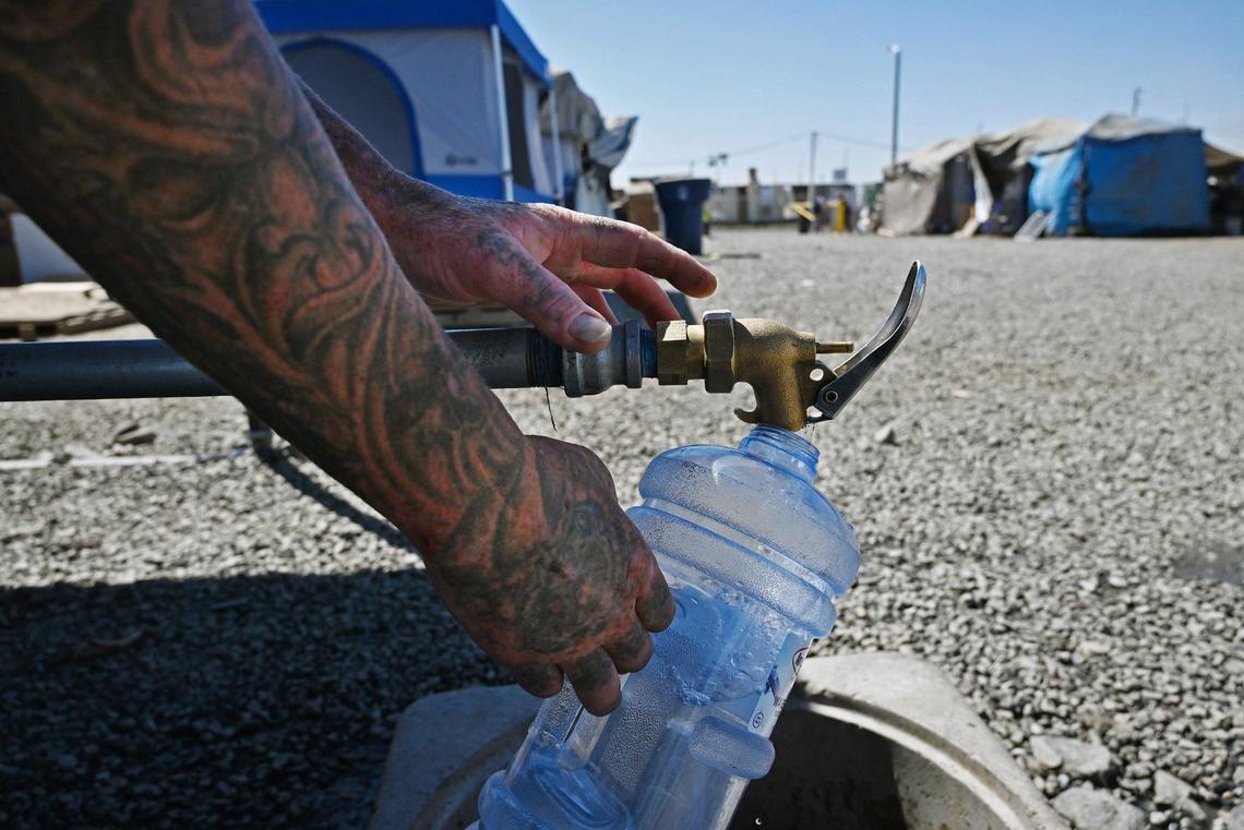 Donny Earp fills a container with water from the only working spigot for the residents at the City of Tulare’s temporary encampment Tuesday, Sept. 10, 2024. Earp said two other spigots were broken by residents and management has locked them until a new system preventing further damage is installed.