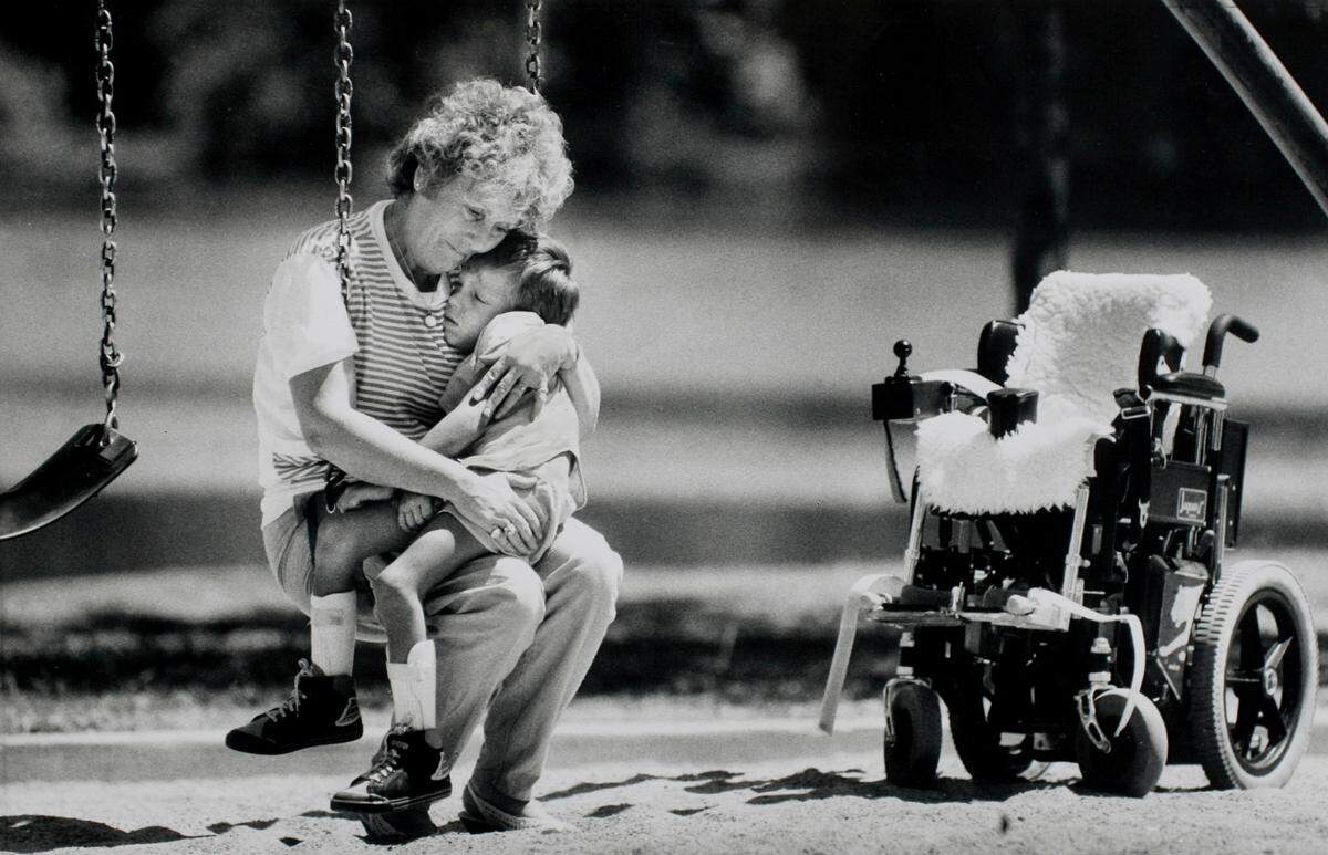 In this 1988 photo, Shirley Patton gently swings her 6-year-old grandson, Shawn, who finds comfort in her arms and a brief respite, at least momentarily, from his electric wheelchair. The boy suffered from muscular dystrophy.