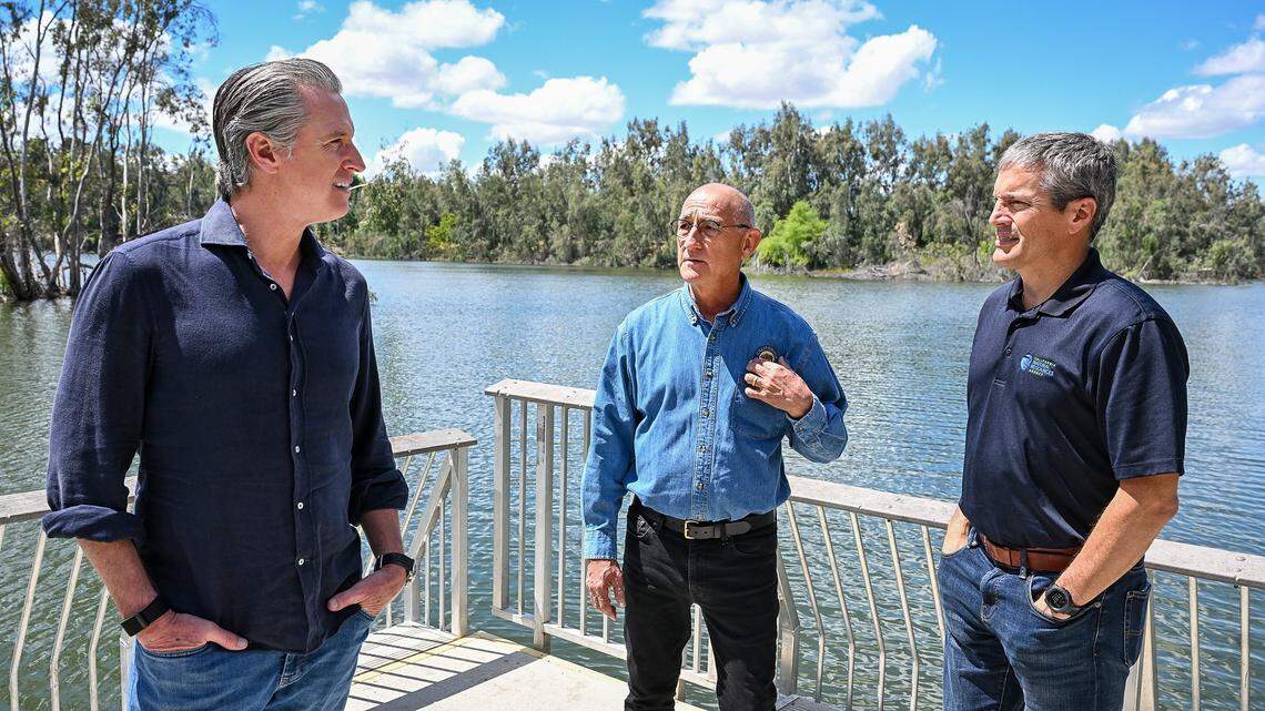 California Gov. Gavin Newsom, left, talks with California State Parks Director Armando Quintero, center, and California Natural Resources Secretary Wade Crowfoot  on the Sycamore Island fishing dock along the San Joaquin River Parkway in Madera County after the governor announced the expansion of the state park system at the site on Wednesday, April 22, 2026. 