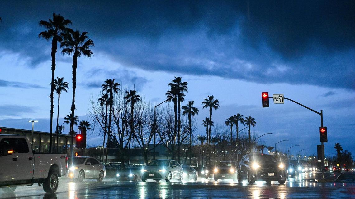 Evening commuters cross Herndon Avenue at Palm in Fresno as dark clouds form across the sky following heavy rain on Thursday, Feb. 13, 2025. Bands of clouds brought in strong thunderstorms through the area with showers possible through Friday.