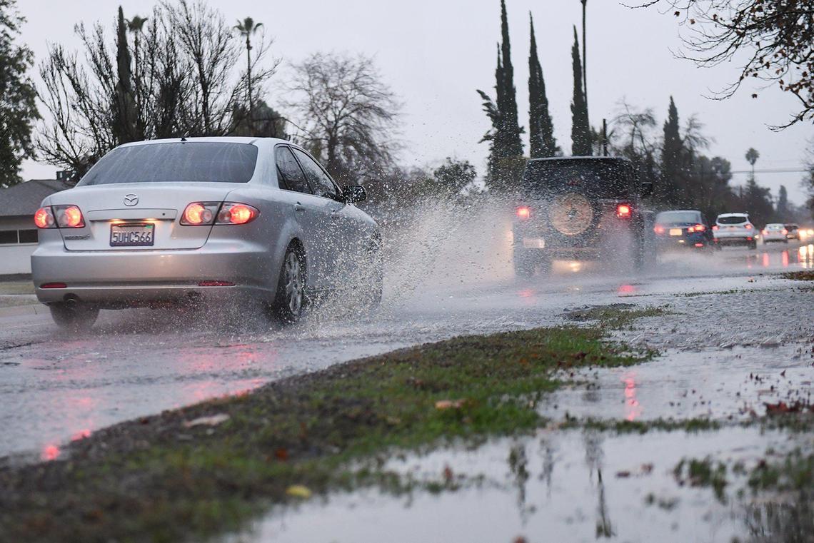 Vehicles splash through standing water along Fruit Avenue north of Ashlan Avenue Thursday evening, Dec. 23,2021 in Fresno.