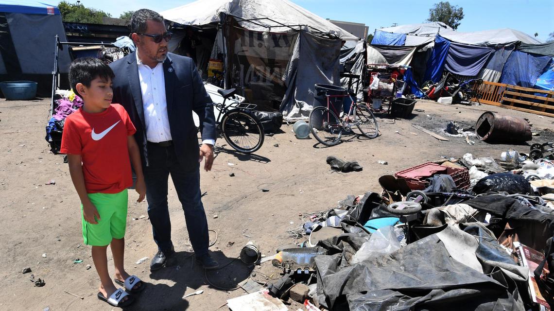 Councilmember Miguel Arias with son Diego, 9, tour a homeless encampment near California Avenue and Monterey Street, July, 22, 2021, as code enforcement inspectors and police officers inspected the site, adjacent to Freeway 99.