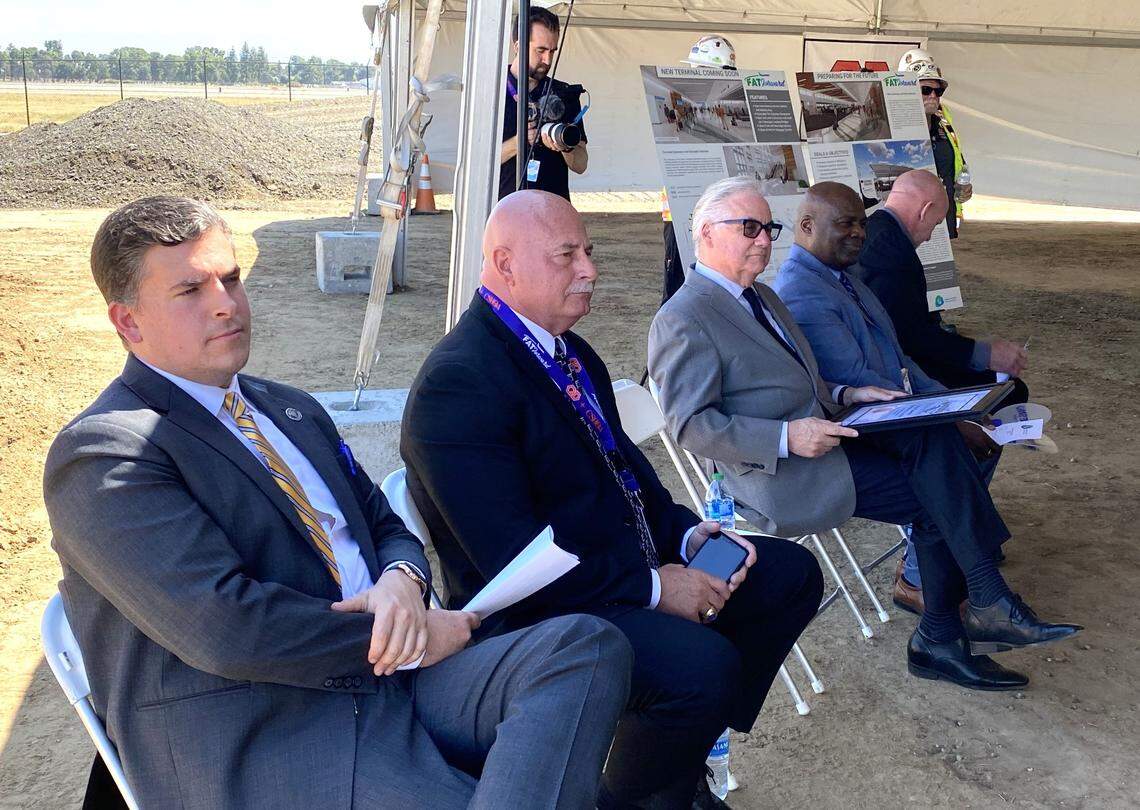 Fresno City Council President Tyler Maxwell, left, Mayor Jerry Dyer, Assemblymember Jim Patterson and Fresno airports director Henry Thompson listen while Rep. Jim Costa spoke at a groundbreaking for the expansion of Fresno Yosemite International Airport on Friday, May 19, 2023. In the background are posters illustrating the terminal expansion.